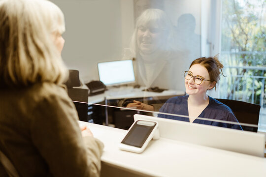 Smiling female medical worker assisting senior patient at reception desk in hospital