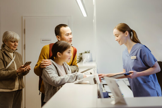 Smiling female healthcare worker assisting girl with father while booking appointment at hospital