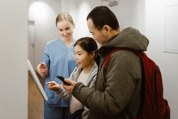 Girl booking appointment while using kiosk with father and nurse in hospital
