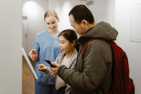 Girl booking appointment while using kiosk with father and nurse in hospital