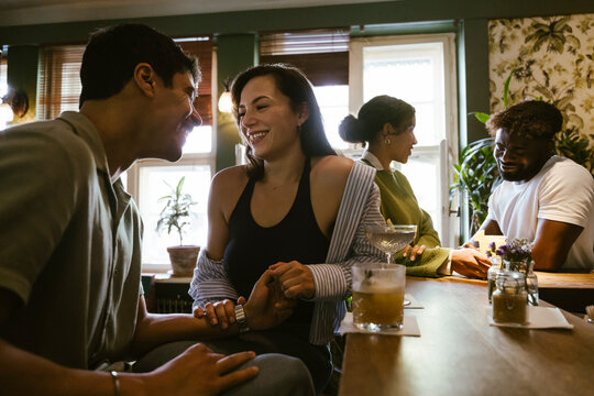 Happy couple holding hands while talking to each other on date at bar