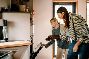 Woman wearing mitt while son opening oven in kitchen at home