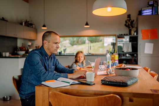 Focused businessman working on laptop while sitting near dining table at home