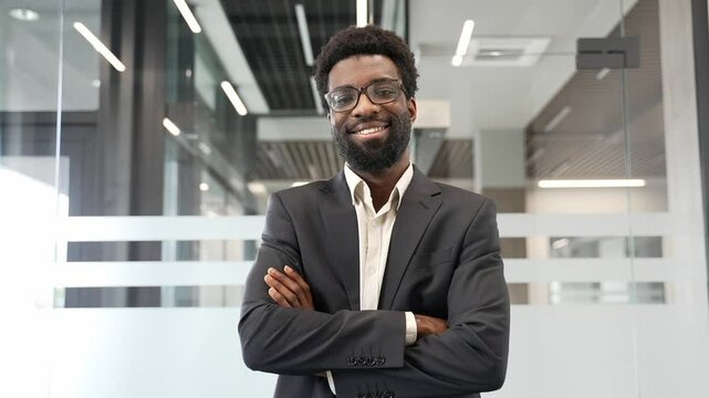 Portrait of African American businessman confidently smiling with crossed arms in a modern office. Successful entrepreneur in glasses looking at camera. Professionalism, success, and upbeat attitude