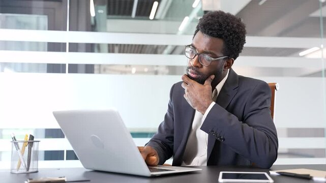African American businessman deep in thought working on laptop in modern office. Thoughtful confident entrepreneur thinking about problem solving sitting at workplace or is busy with a startup project