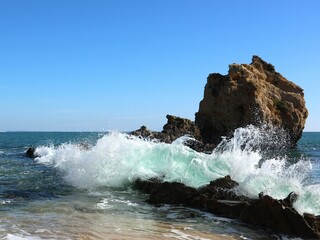 Waves crashing against coastal rocks under a blue sky.