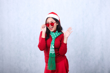 beautiful woman wearing red sweater with Santa hat and scarf celebrating merry christmas and new year, cheerful to camera hand holding red glasses and greeting forward, isolated on white background