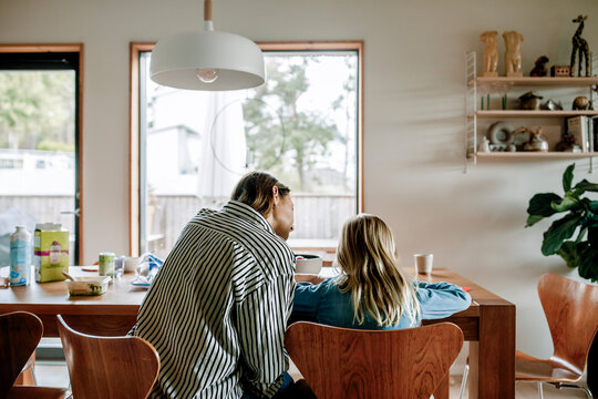 Rear view mother guiding son doing homework while sitting on chair near table at home