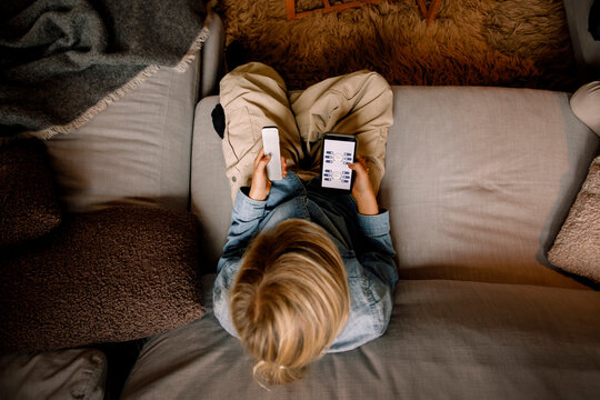 Directly above shot of blond boy holding remote while sitting on sofa at home