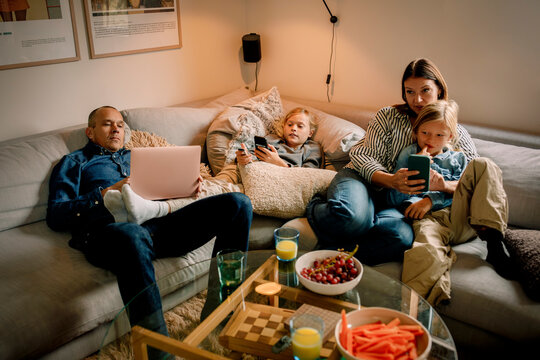 Family spending leisure time using wireless technologies while sitting on sofa at home