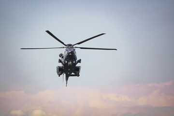 Front view of a military helicopter is hovering in the sky at an airshow. Cloudy sky in the...