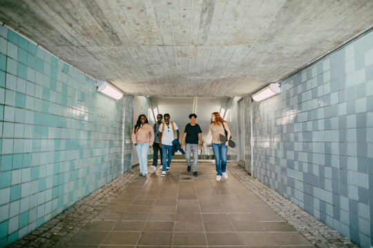 Full length of multiracial male and female friends walking in underground tunnel
