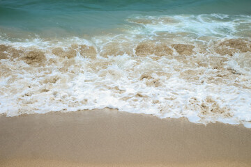 Soft waves of blue sea with foam on golden white sandy beach. Wave background
