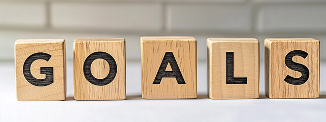 Wooden blocks spelling "GOALS" sit on a reflective wooden surface with a softly lit background.