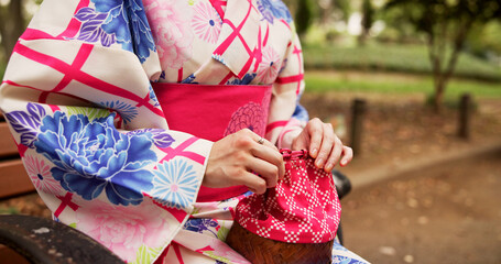 Woman, hands and kimono in park with bag, traditional fashion and relax with indigenous style in Japan. Girl, purse and outdoor in Tokyo with culture, drawstring kago and elegant aesthetic on bench