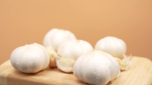 A bunch of white garlic bulbs are sitting on a wooden cutting board. The bulbs are all different sizes and are arranged in a row. Concept of freshness and natural beauty. Garlic rotates on an orange b