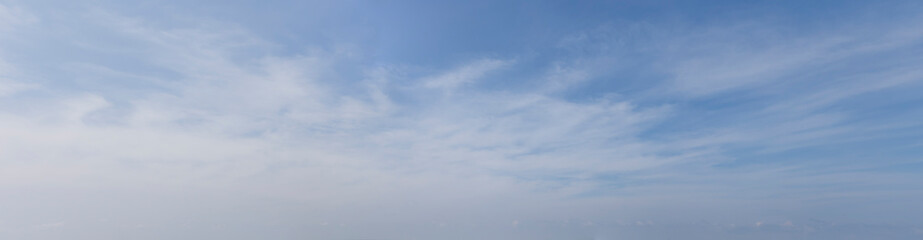 Wide-angle landscape photograph capturing a calm blue sky with soft white cirrus clouds, evoking tranquility and serenity.
