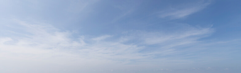 Wide-angle landscape photograph capturing a calm blue sky with soft white cirrus clouds, evoking...