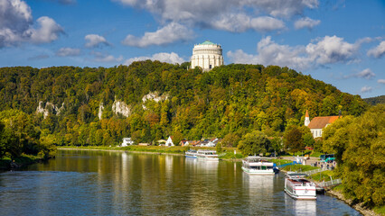 view of the danube near kelheim with excursion boats on the riverbank and autumnal forest in the sunshine