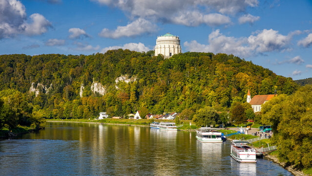 view of the danube near kelheim with excursion boats on the riverbank and autumnal forest in the sunshine