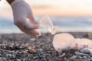 A man's hand removes a plastic cup and debris from the beach close-up
