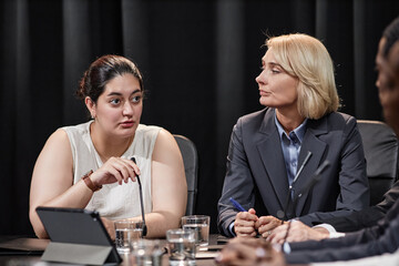 Middle Eastern female politician asking colleague question adjusting microphone while debating during committee meeting against black curtain in conference room