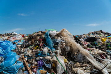 A vast amount of waste, including plastic and debris, tarnishes the landscape under a blue sky, underscoring the pressing need for better waste management and recycling