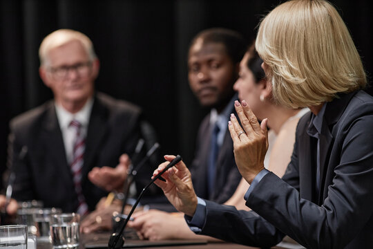 Rear view of female official speaking into microphone asking politician question during political debate or press conference meeting room, copy space