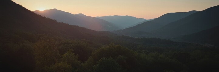 Obraz premium a scenic view of a mountain landscape during sunset or sunrise. The sky is a gradient of warm colors, transitioning from orange near the horizon to a lighter blue higher up