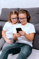 Two girls use a parental control app on a phone, playing a kids' game and sharing a gadget while relaxing at home. Perfect for themes about safe content, parental control, and technology.
