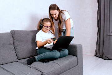 A young mother assisting her little daughter with online payments using a laptop. A cozy moment of family life, e-commerce, and teaching kids about online transactions at home.