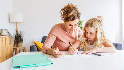 Happy young mother helping her daughter doing school homework at home - Education and childhood...