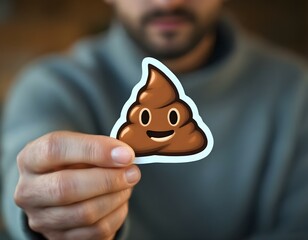 Enshittification concept photography. A person is holding a poop emoji sticker, showing it to camera.