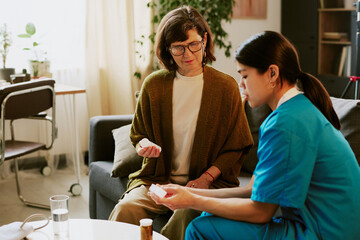 Healthcare professional assisting elderly woman with medication instruction, senior woman seated on...