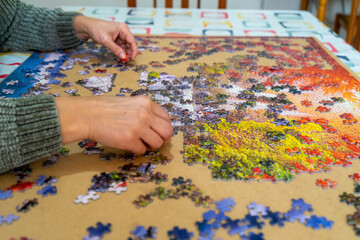 Horizontal close-up image of a woman's hands searching for the right piece to solve the puzzle,...