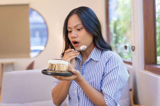 Happy woman opens mouth wow, staring at cake in hand, spoon in hand enjoying her favorite dessert.  Proper nutrition, fast food, unhealthy options. Junk food makes you fatter.