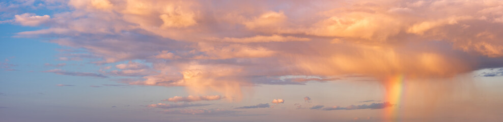 Panoramic background of sky with rain shower, rainbow and orange clouds at sunset