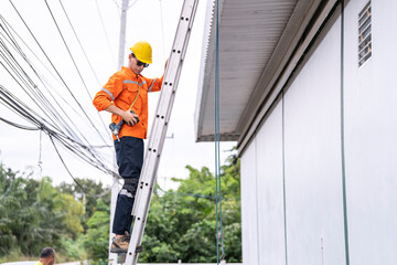 A safety conscious technician in an orange safety jacket and yellow hard hat ascends a metal ladder...