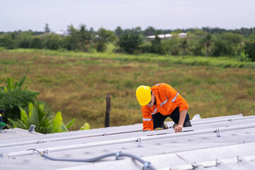 Worker in an orange safety uniform and helmet carefully inspecting a metal rooftop under natural daylight. Depicts diligence, precision, and professional commitment in construction and maintenance.