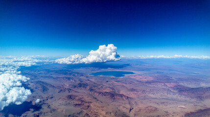 "A panoramic view of the Arizona desert with mountains and blue sky, with one large white cloud in front of it, and Lake Mead visible below on the horizon, shot from high above."