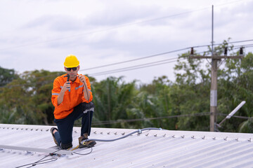 Technician in an orange safety uniform and helmet handling an electrical cable on a rooftop. Represents safety, professionalism, and expertise in renewable energy installations and maintenance work.