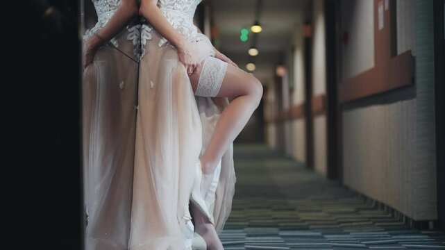 Sexy seductive sensual bride woman in a wedding dress is adjusting stockings lingerie. She is standing in hotel hallway, isolated cinematic shot