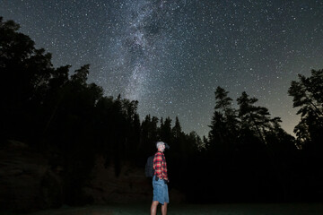 Fototapeta premium Night hiking, man with night vision goggles on his head in night forest with starry sky.