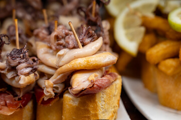 Typical snack of Basque Country, pinchos or pinxtos skewers with small pieces of bread, sea food, eggs, cheese, jamon served in bar in San-Sebastian or Bilbao, Spain, close up