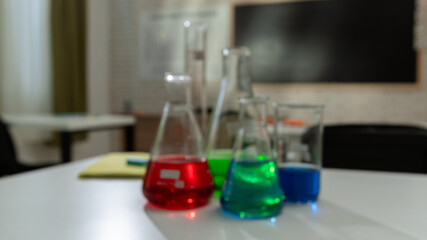 Empty school chemistry classroom with desks, chairs and chalkboard, workspace for teaching and studying. Glass bottles with colorful liquids close up.