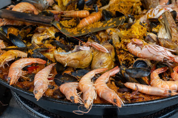 Street food in France, fresh prepared colorful paella with rice and sea food in big pan on street market ready to eat