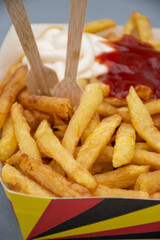 Belgian street and fast food, paper box in colors of Belgian flag with fried potato frit chips and ketchup and mayonnaise sauсe