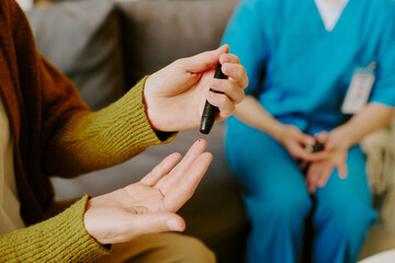 Obraz premium Elderly person checking blood sugar levels with glucometer while sitting on couch, assisted by healthcare professional wearing blue scrubs and holding medical report