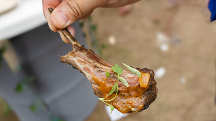 A hand is holding a barbecued lamb. Quick and tasty meal during cold season. The lamb is well seasoning with sauce and pepper. Top with cilantro. Dip with ketchup. Grill around 15 mins with high fire