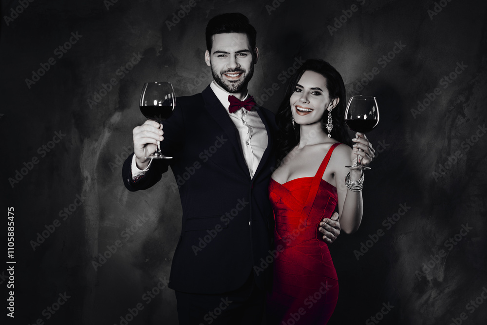 Poster portrait of cheerful festive couple having wineglasses with red wine in raised hands looking at came